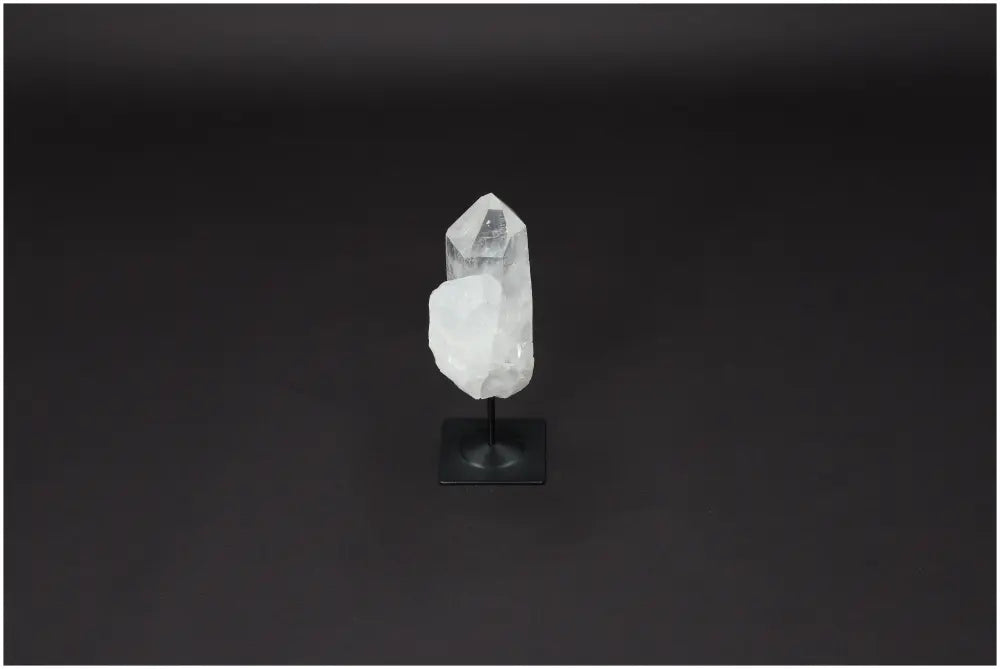 Clear Lemurian Quartz on metal stand against dark background, known for purification and harmonizing energy.