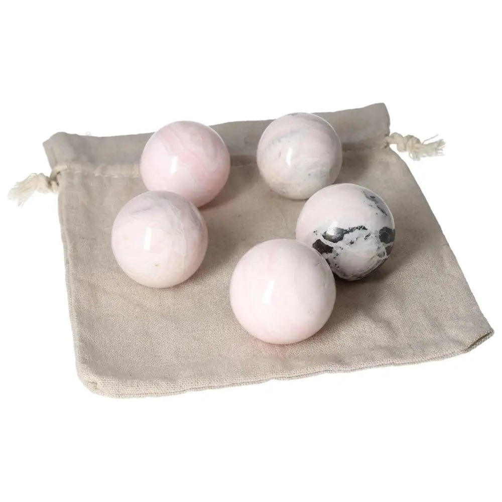 Five mangano calcite spheres on a beige pouch, promoting peace and creativity with their powerful healing properties.
