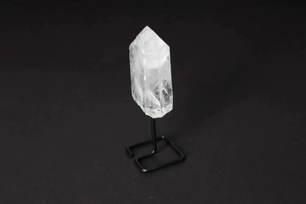 Clear Quartz crystal point on a black stand, ideal for meditation and energy alignment, set against a dark background.