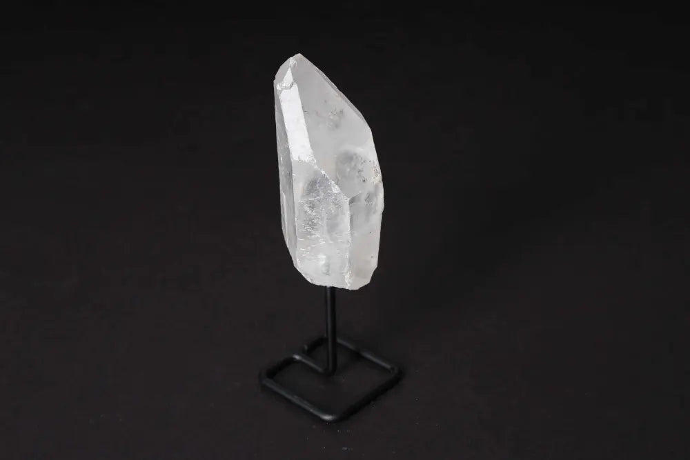 Clear Quartz Point on stand, known for amplifying energy and clarity, ideal for meditation and energy work, against dark background.
