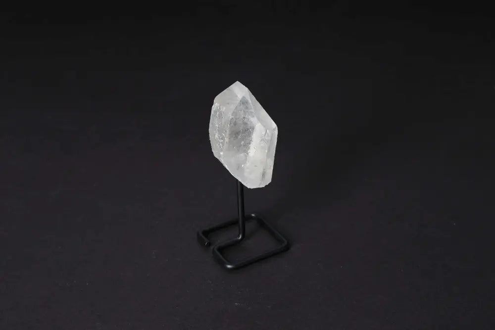Natural clear quartz point on stand, used for energy amplification and clarity, against a dark background.