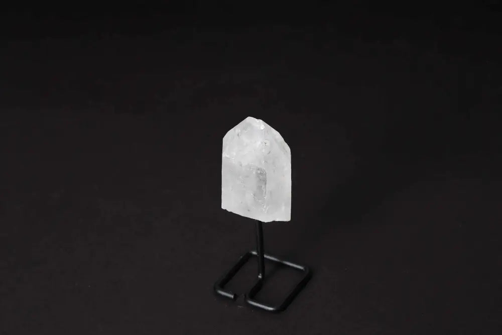 Natural Clear Quartz Point on a black stand for energy amplification and meditation focus against a dark background.