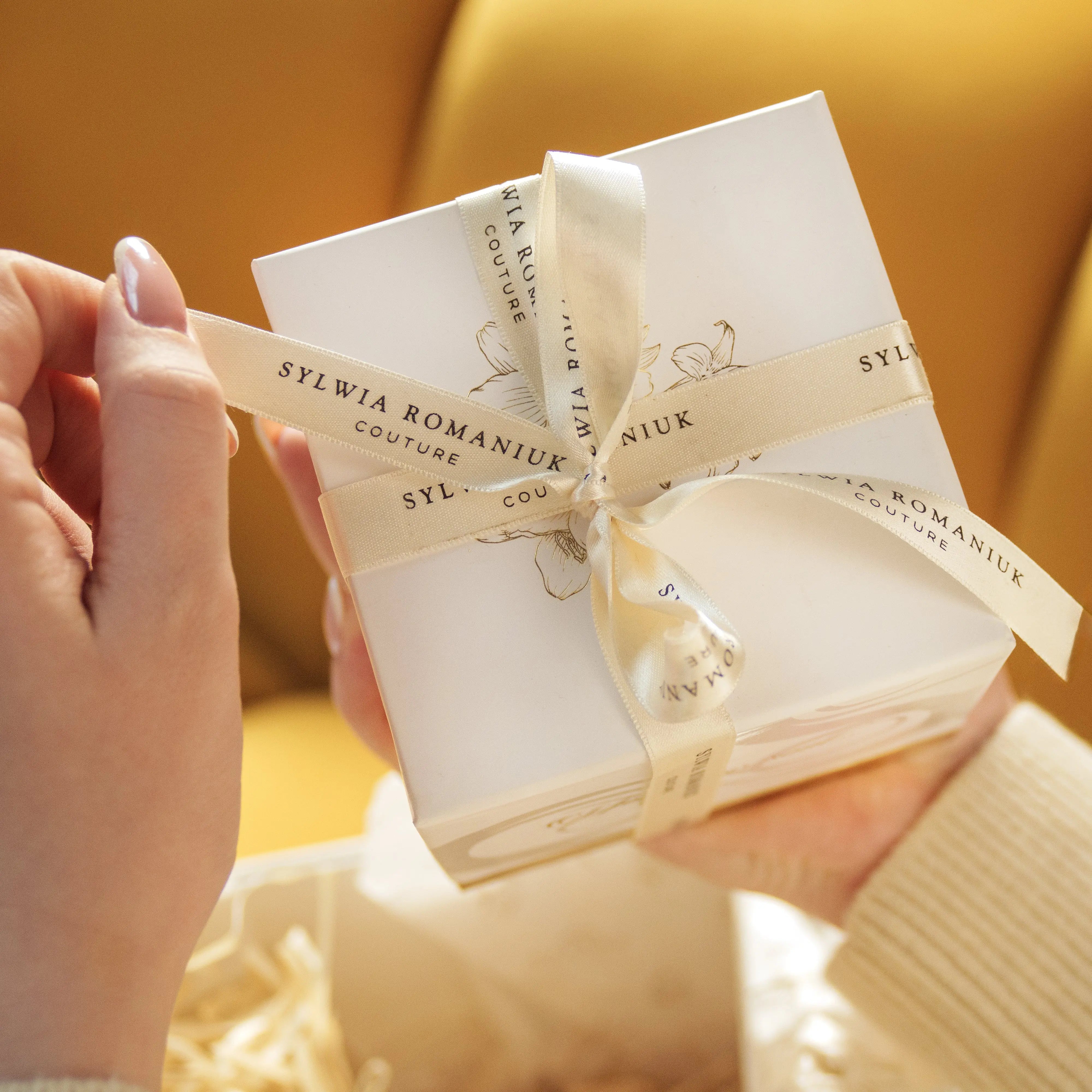 Person holding Sylwia Romaniuk HOME candle gift box wrapped with elegant ribbon, perfect for elevating home or gifting experiences.