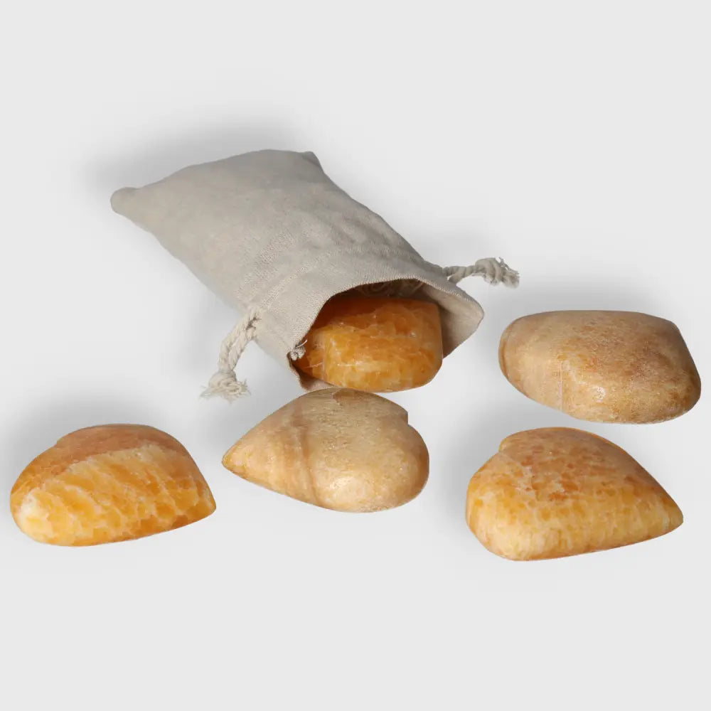 Orange Calcite Heart gemstones spilling from a beige pouch, symbolizing love and joy with vibrant, uplifting energy.