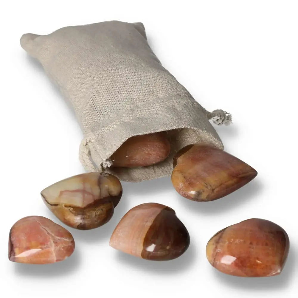 Collection of polished Peach Calcite Hearts with a soft peach hue beside a beige fabric pouch, symbolizing love and emotional renewal.