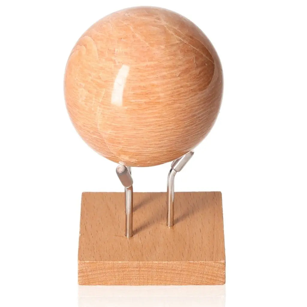 Peach Moonstone Sphere on wooden stand, known for its calming energy and soft peach hue, promotes intuition and emotional healing.