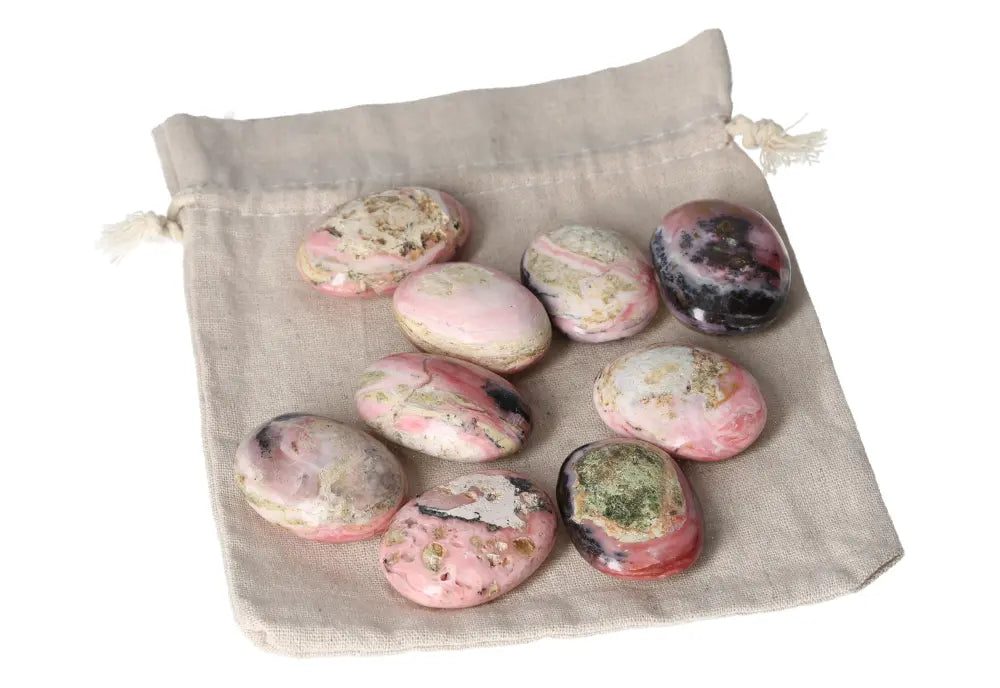 Collection of pink opal palmstones on a beige drawstring bag, showcasing soothing pastel hues and smooth surfaces for emotional healing.