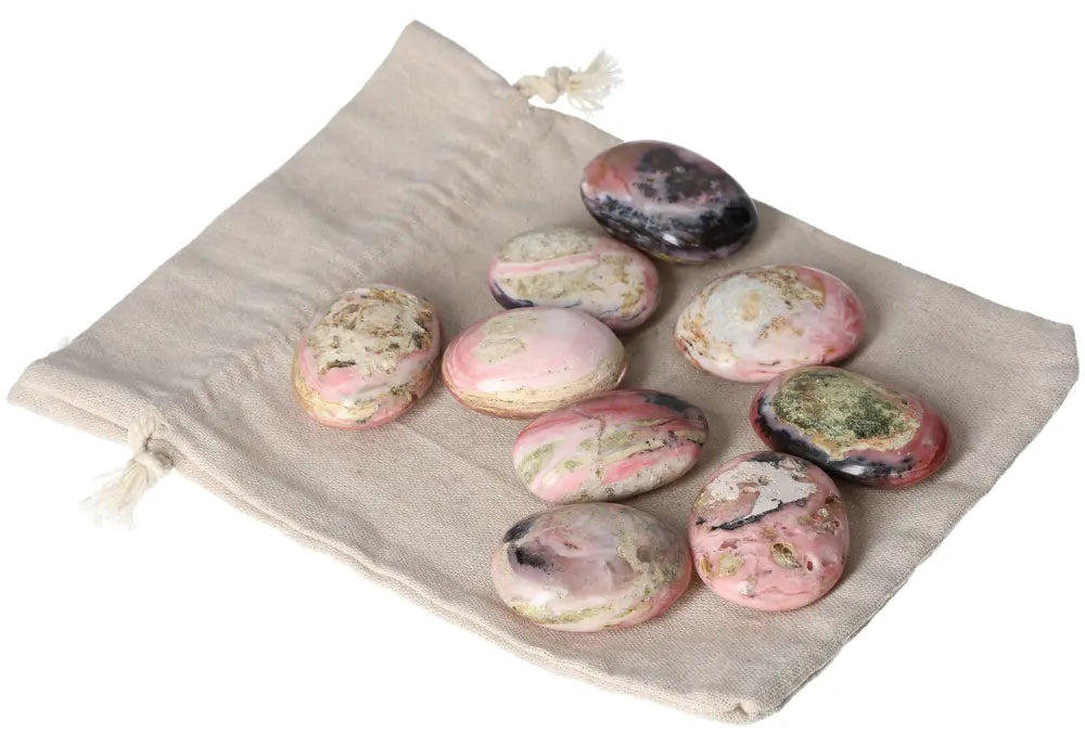 Collection of pink opal palmstones with pastel hues displayed on a beige fabric bag, promoting emotional healing and personal transformation.