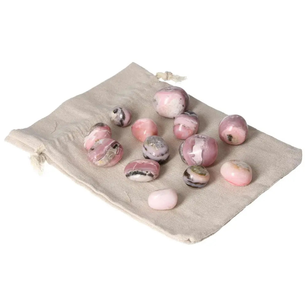 Pink opal tumbled stones on a beige fabric pouch, showcasing their soft pastel pink hues and smooth, soothing texture for emotional healing.