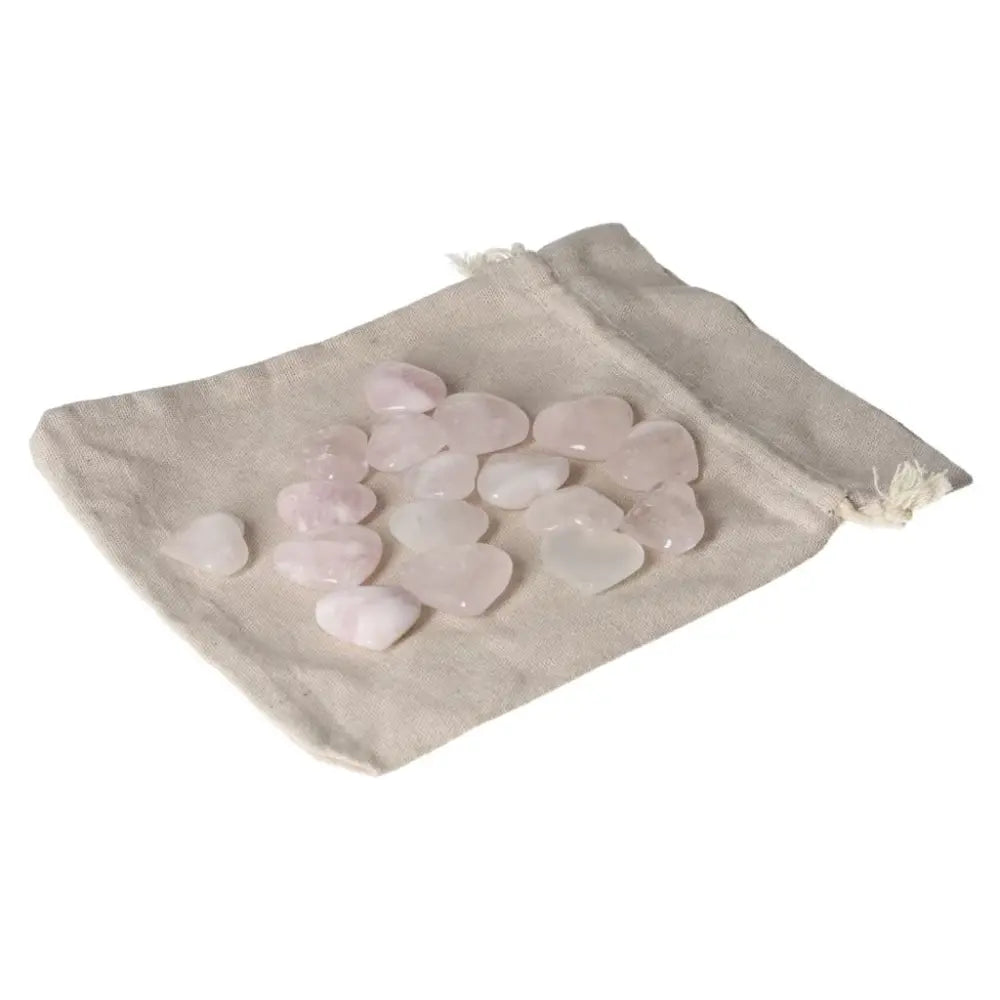 Pink quartz small heart stones spread on a beige cloth pouch, showcasing their delicate hue and polished finish.