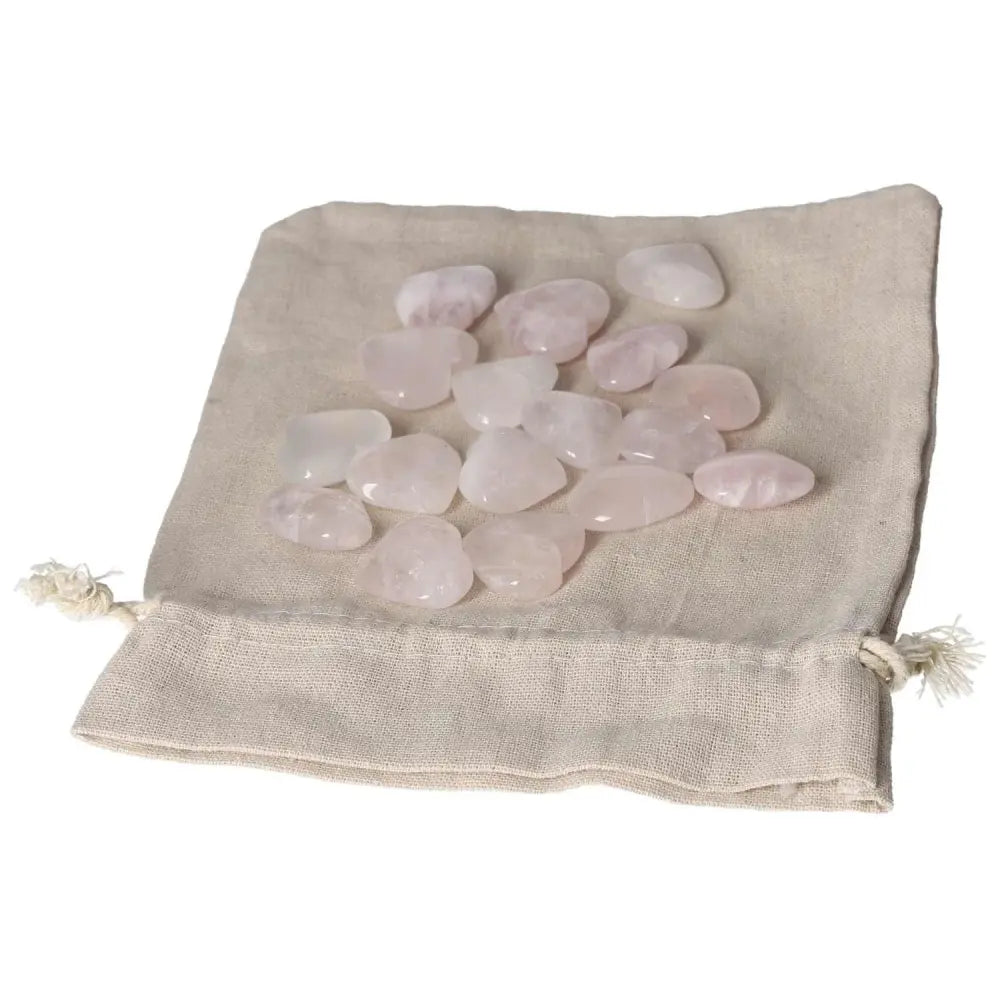Collection of small pink quartz hearts on a beige cloth bag, showcasing natural gemstone beauty and gentle pink hues.