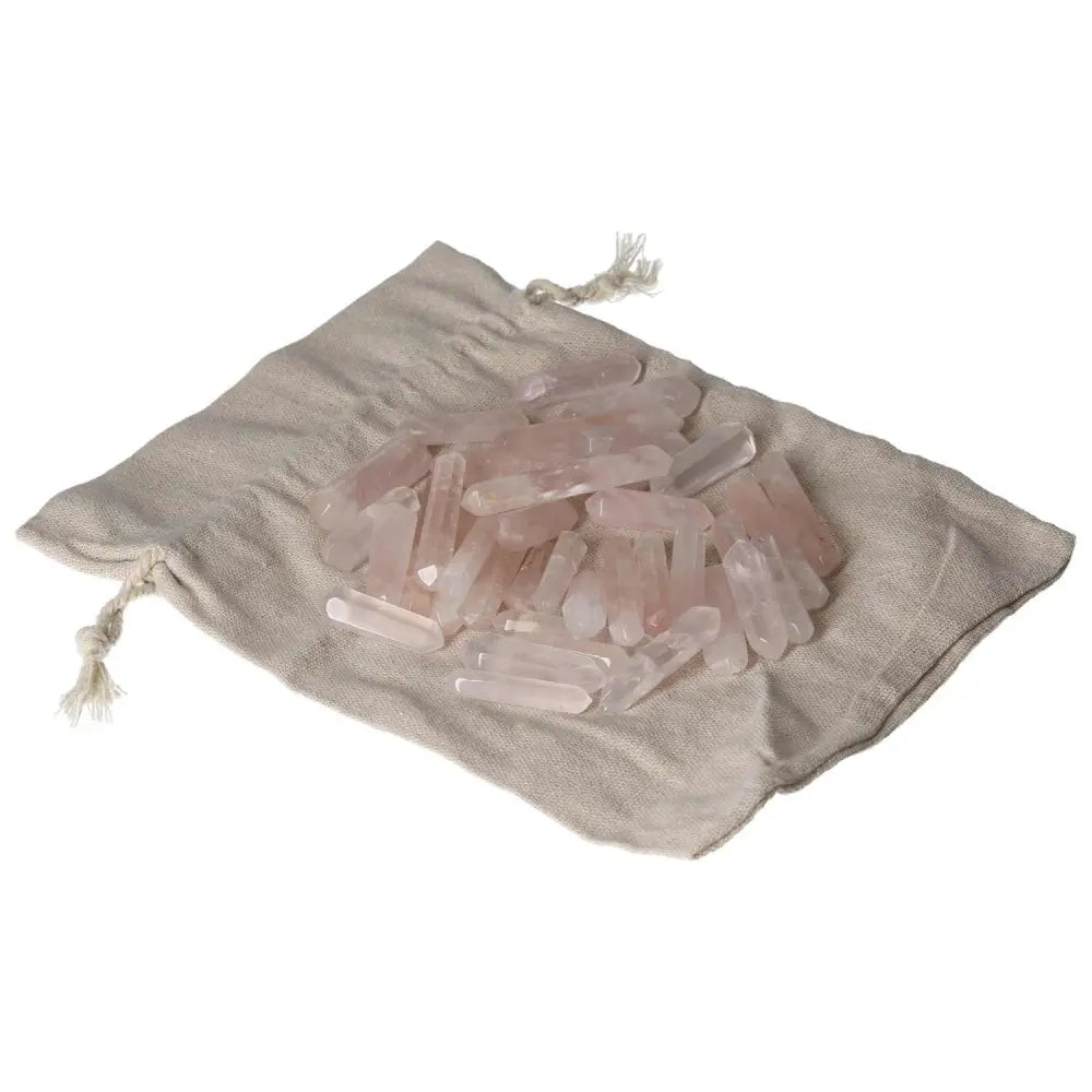 Pile of small pink quartz sticks on a beige fabric bag, perfect for healing and decorative purposes.