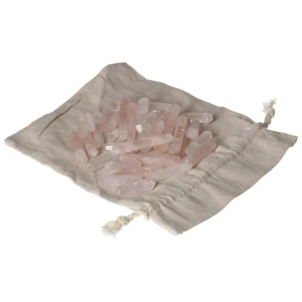 Pink quartz small sticks arranged on a beige cloth bag, showcasing their natural beauty and crystal clarity.