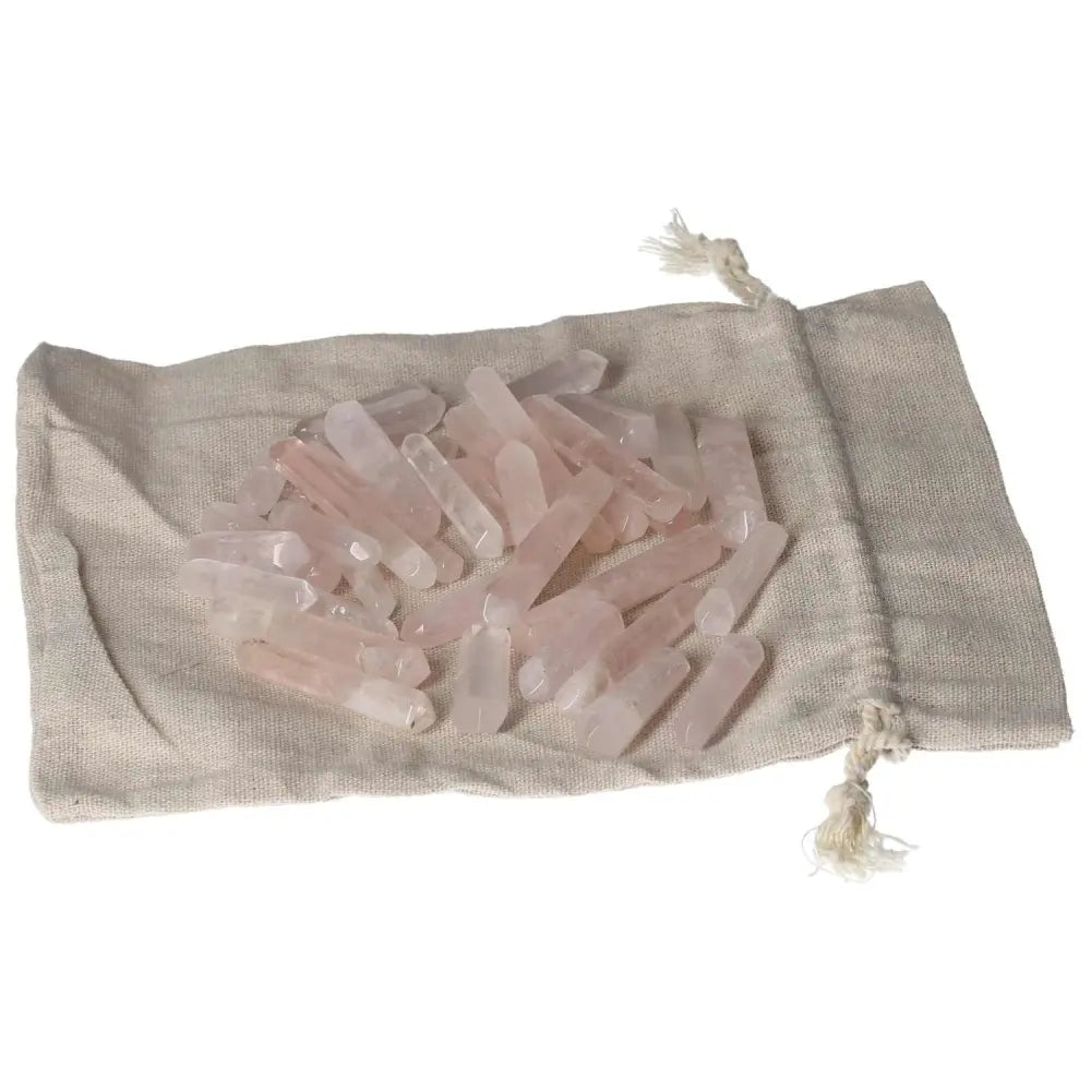 Assorted pink quartz small sticks on a beige drawstring bag, perfect for jewelry making or healing rituals.