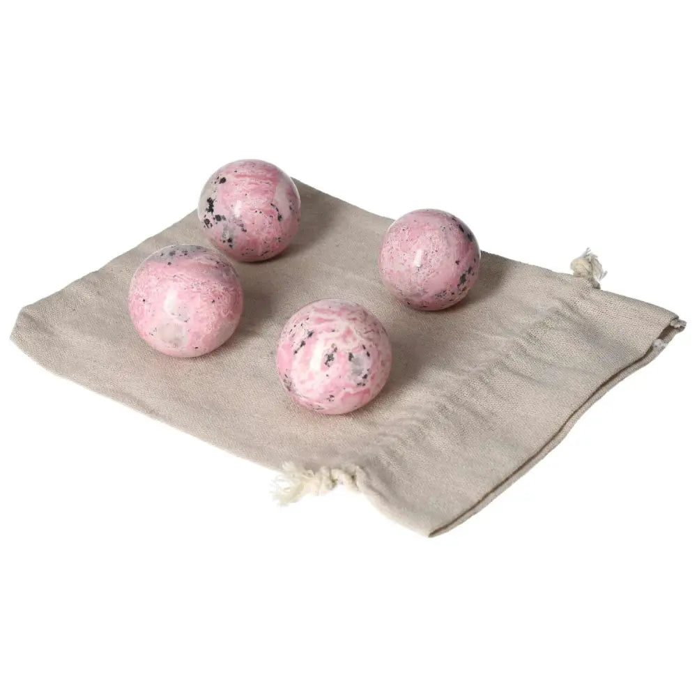 Four polished Rhodonite spheres on a beige cloth, showcasing vibrant pink hues and unique patterns, symbolizing healing and positive energy.