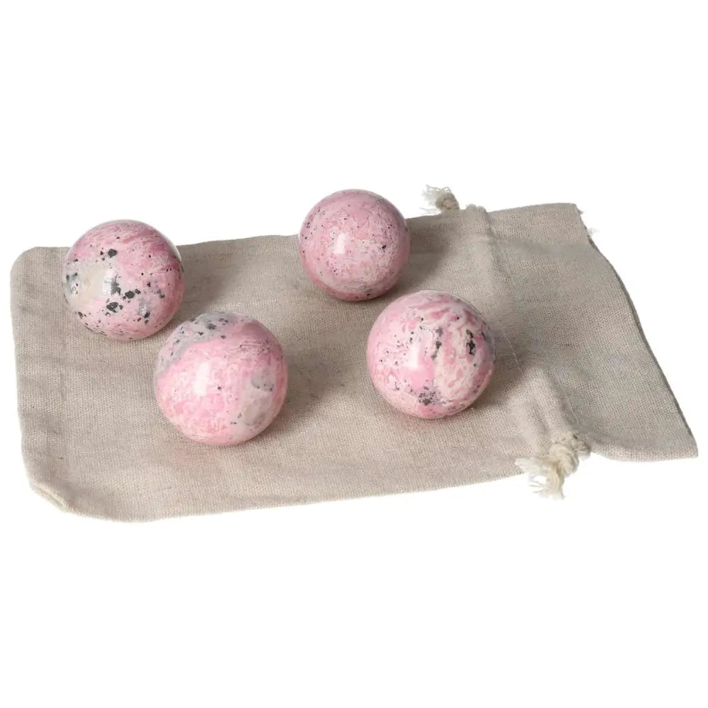 Four rhodonite spheres displayed on a cloth pouch, showcasing vibrant pink color and unique patterns for healing and energy clearing.