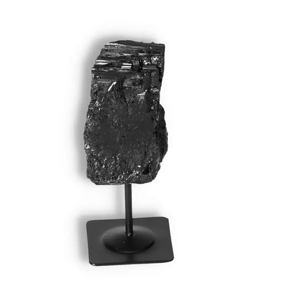 Rough Black Tourmaline on a metal stand by Sylvia Crystals, known for cleansing and transforming negative energies.