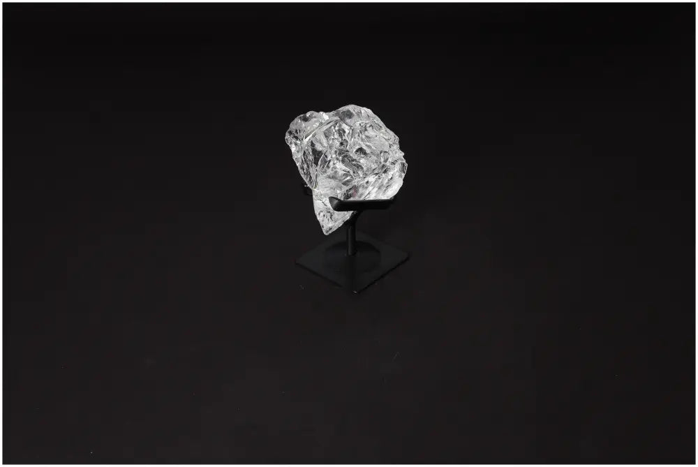 Rough clear quartz crystal on a sleek metal stand for purification and harmonizing energy spaces.