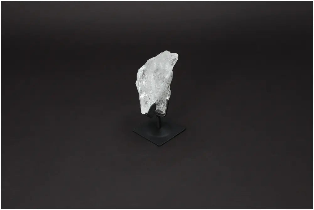 Rough Lemurian Quartz crystal on metal stand by Sylvia Crystals, offering purification and energy, displayed against a dark background.