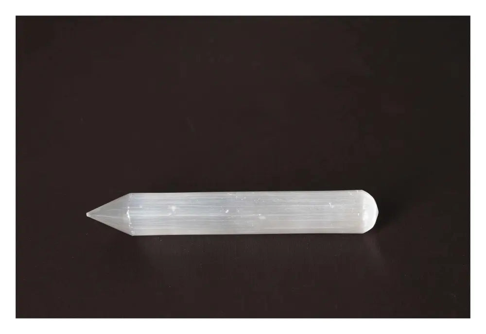 Selenite massage wand with glass-like transparency and natural striations for purifying and soothing energy on dark background.