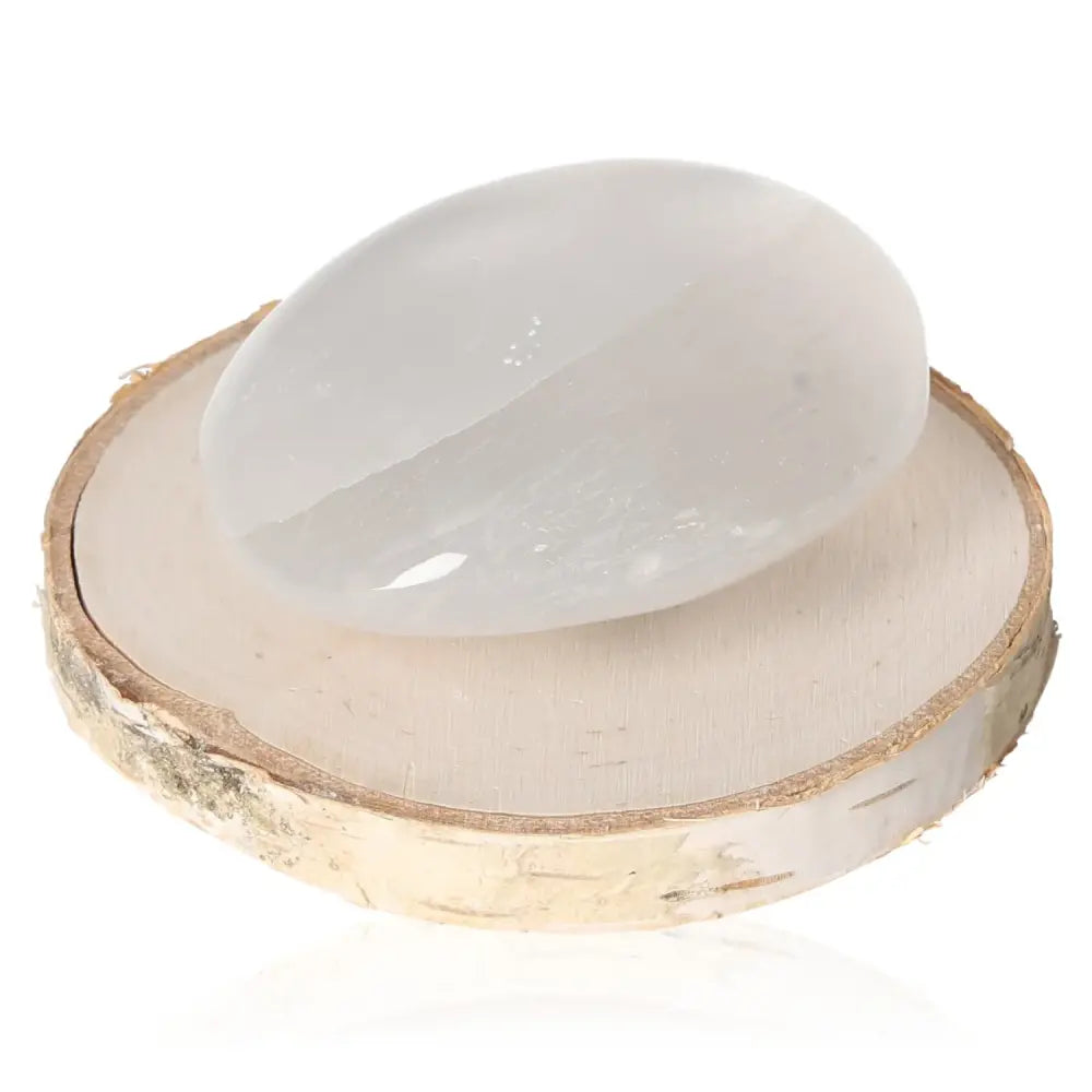 Selenite palmstone 6/7cm with glass-like transparency, capturing light on wooden base, perfect for soothing and harmonious atmosphere.