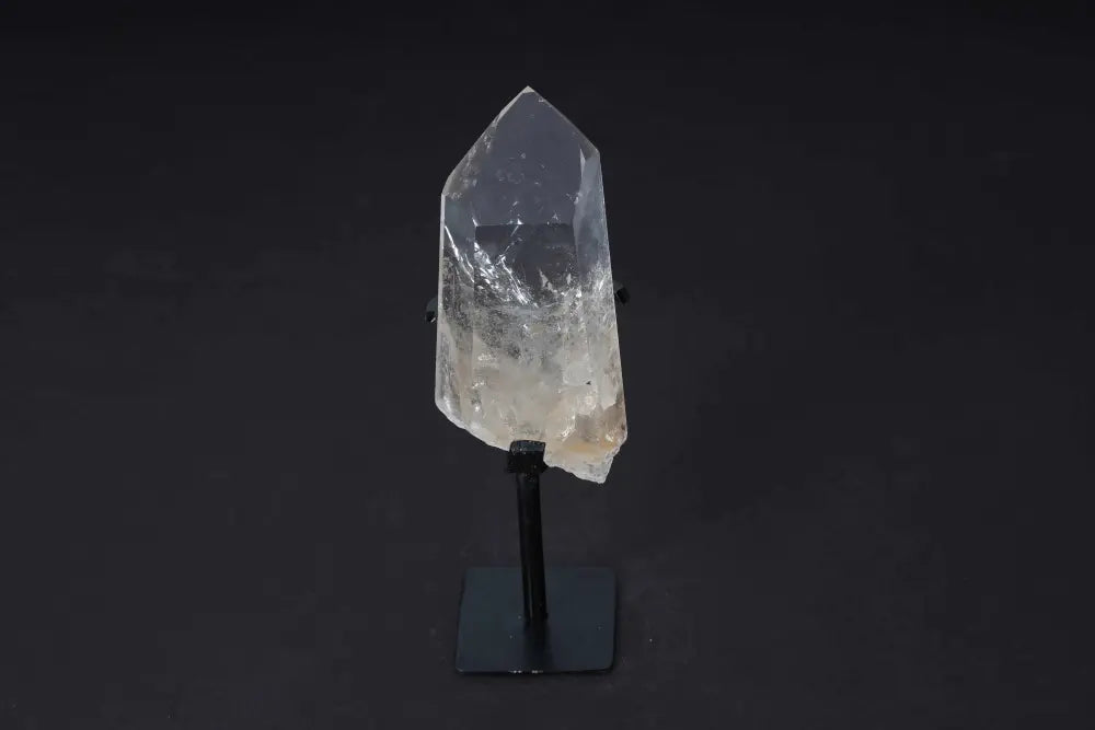 Semi polished clear quartz point with stand, known for energy amplification and clarity, displayed on a sleek modern stand.