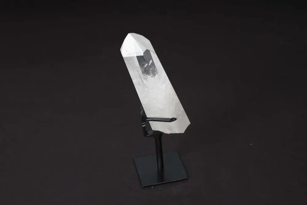 Semi polished clear quartz point on stand, amplifies energy and clarity, ideal for meditation and manifestation, on black background.