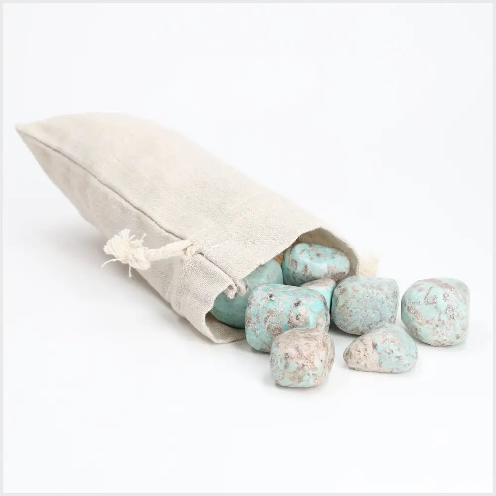 Tumbled Amazonite stones spilling from a beige pouch, showcasing soothing turquoise and green hues, symbolizing courage and truth.