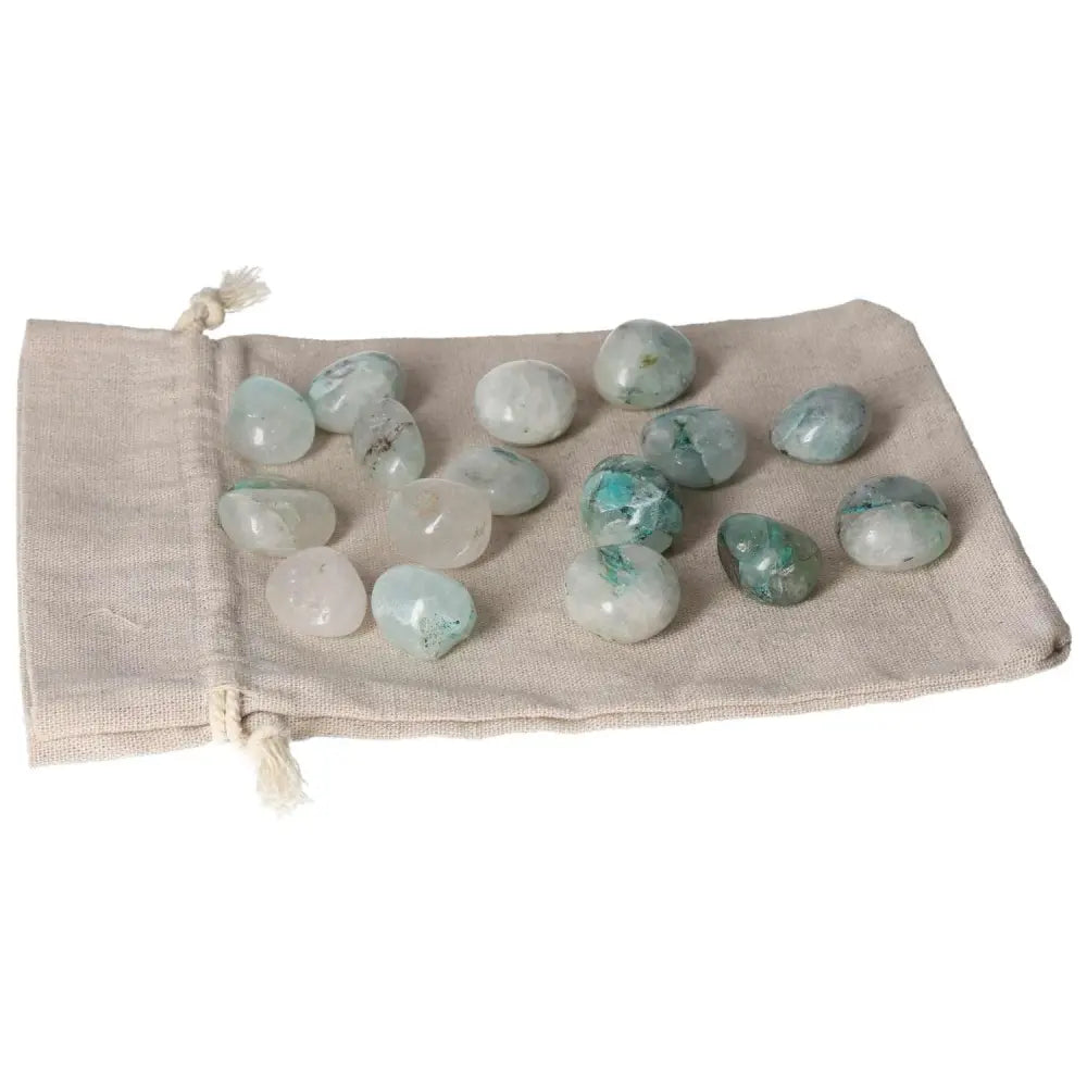 Tumbled Chrysocolla stones on a beige fabric pouch, known for enhancing communication and fostering feminine energy.