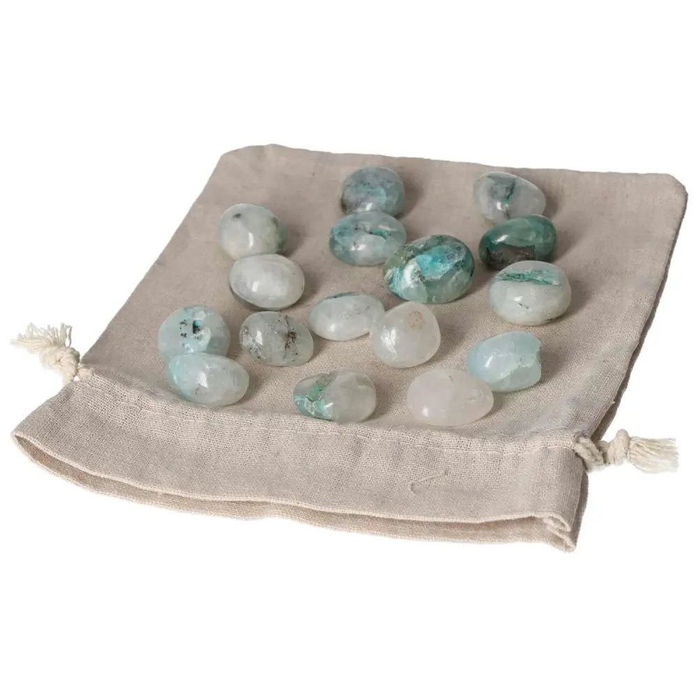 Tumbled Chrysocolla stones on a beige pouch, highlighting their feminine energy and speech-enhancing properties.