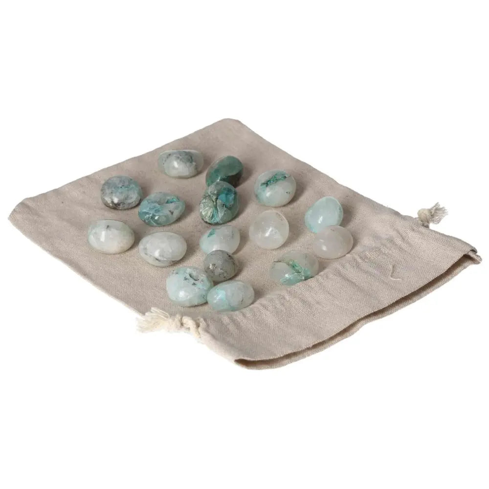 Tumbled Chrysocolla stones with calming blue-green hues on a beige cloth, enhancing communication and emotional understanding through feminine energy.