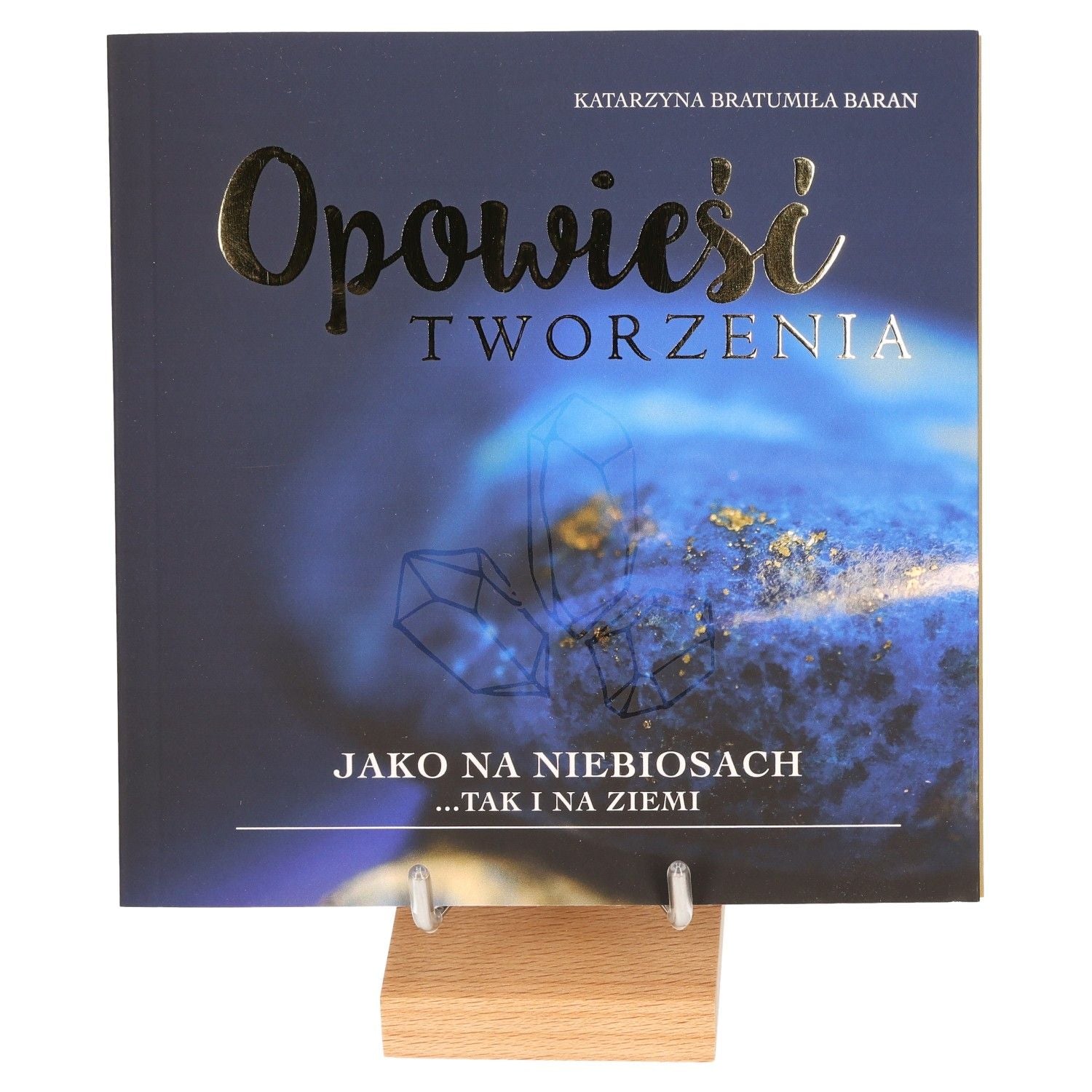 Book cover featuring "Opowieści Tworzenia" with a blue and crystal theme on a wooden stand.