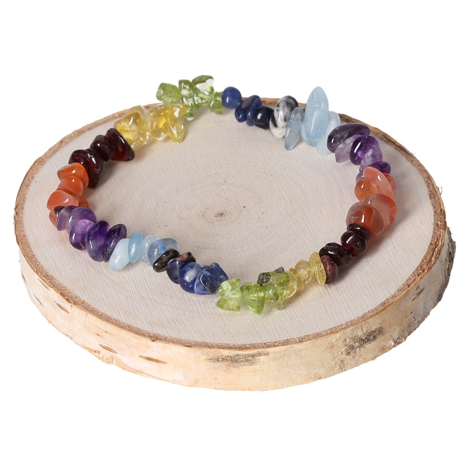 Colorful chakra bracelet made of gemstone chips displayed on a wooden disc for spiritual healing and energy balance.